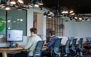 Binnenaanzicht van een modern, gemeubileerd kantoorruimte te huur op Uitbreidingstraat 66, Antwerpen Berchem, met werkende mensen achter computers met hoofdtelefoons.