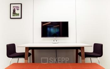 Kantoorruimte te huur op Uitbreidingstraat 66, Antwerpen Berchem met een minimalistisch bureau, twee zwarte stoelen en een rode bank, voorzien van een wand-tv.