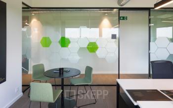 Modern kantoor te huur op Uitbreidingstraat 66, Antwerpen Berchem, met glazen wanden en stijlvolle groene stoelen rond een tafel, ideaal voor zakelijke bijeenkomsten.