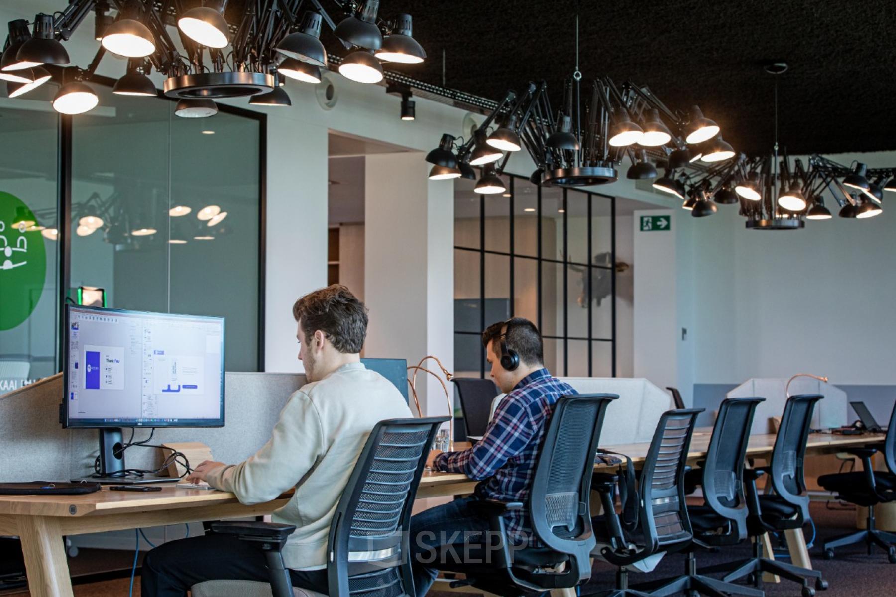 Binnenaanzicht van een modern, gemeubileerd kantoorruimte te huur op Uitbreidingstraat 66, Antwerpen Berchem, met werkende mensen achter computers met hoofdtelefoons.