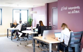 Modern office space with people working at desks, located at De Keyserlei 58-60 in Antwerp Center. Bright room with large windows and inspirational wall text.