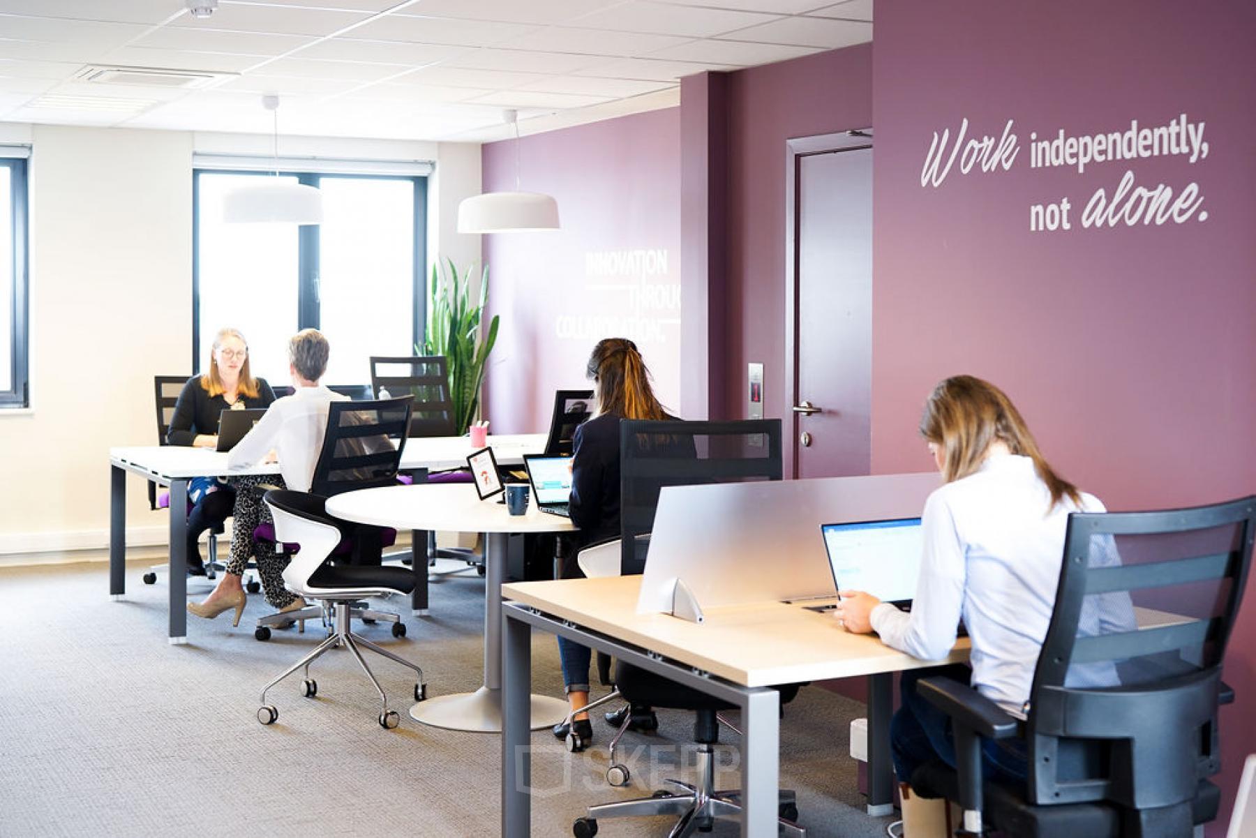 Modern office space with people working at desks, located at De Keyserlei 58-60 in Antwerp Center. Bright room with large windows and inspirational wall text.