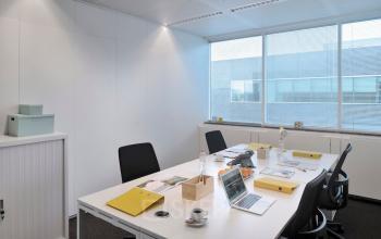 Bright office space with a large window, four desks, chairs, and office supplies in Antwerp Center, ideal for rent office space seekers.