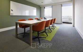 Vergaderzaal met witte muren, een lange tafel en acht oranje stoelen bij Noorderlaan 147, kantoorruimte te huur in Antwerpen Merksem.