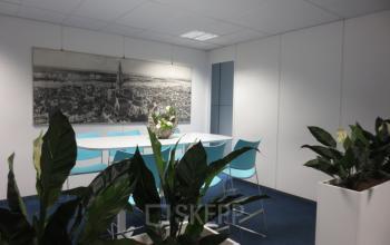 Modern conference room with a long white table, blue chairs, and decorative plants at Boomsesteenweg 690, Antwerp Wilrijk.