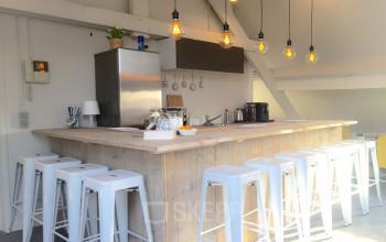 Modern pantry in an office to rent at Grote Hondstraat 44, Antwerp Zurenborg, featuring a wooden bar with white stools and hanging industrial lights.