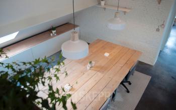 Bright, modern office to rent in Antwerp Zurenborg at Grote Hondstraat 44. Features a spacious wooden table, industrial pendant lights, and minimalist design, suitable for collaborative work.