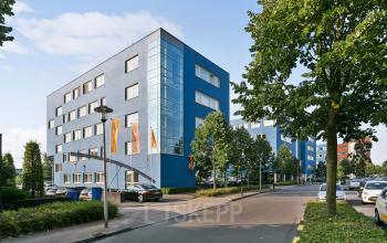 Blue office building located at Linie 580-596, Apeldoorn. The building has multiple windows and is surrounded by trees and parked cars.
