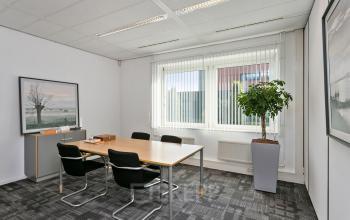 Bright office space rental at Linie 580-596 Apeldoorn, featuring a meeting table, chairs, and large window with blinds.