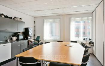 Bright conference room at Linie 580-596 in Apeldoorn with a large meeting table, chairs, and a kitchenette in the corner.