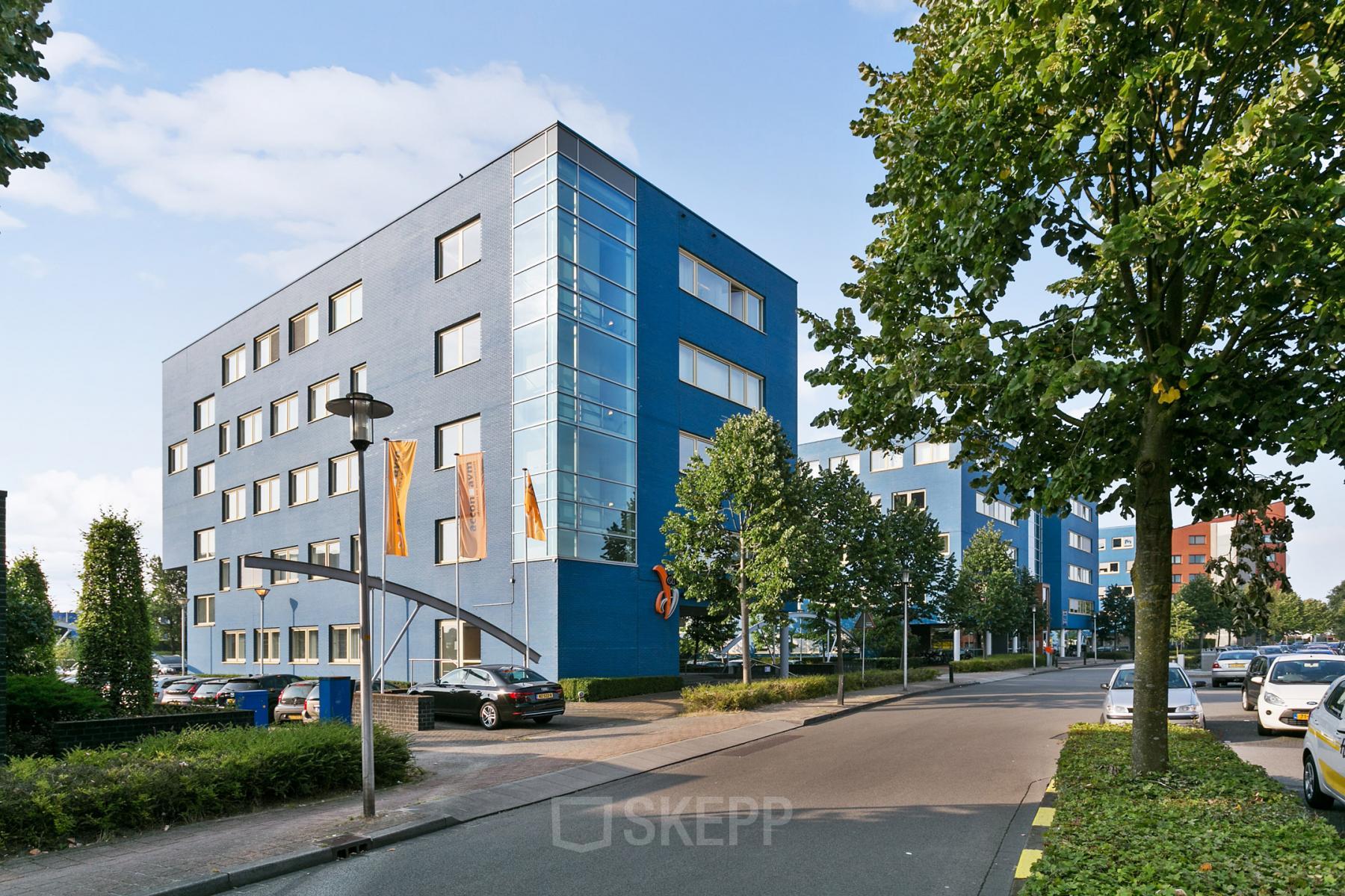 Blue office building located at Linie 580-596, Apeldoorn. The building has multiple windows and is surrounded by trees and parked cars.