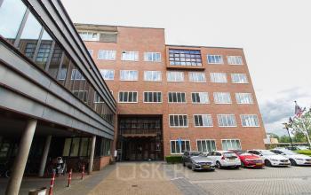 Modern office building exterior at Het Rietveld 55A, showcasing an appealing office space rental opportunity in Apeldoorn with parked cars and a clear entrance.