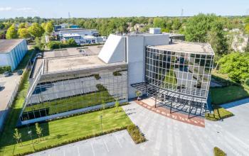 A modern office building at Landdrostlaan 51, Apeldoorn, featuring large glass windows and ample parking space, ideal for office space rental.