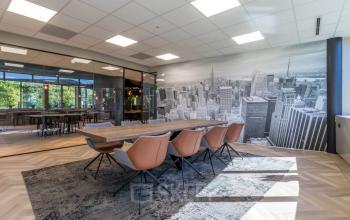 At Landdrostlaan 51, Apeldoorn, a stylish office space is available for rent, featuring a conference room with a cityscape mural, modern chairs, and ample natural light.