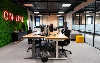 A modern office space for rent at Landdrostlaan 51, Apeldoorn, featuring multiple workstations, a green wall with 'ON-LINE' sign, and sleek glass partitions.