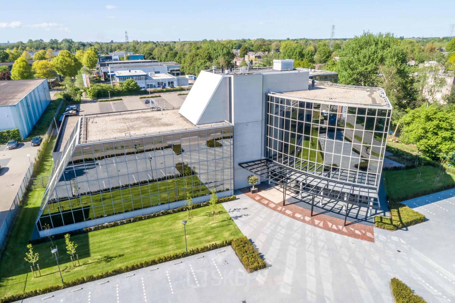 A modern office building at Landdrostlaan 51, Apeldoorn, featuring large glass windows and ample parking space, ideal for office space rental.