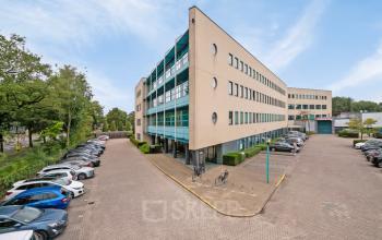 Exterior view of office space for rent at Lange Amerikaweg 55-61, Apeldoorn, featuring a large modern building with ample parking.