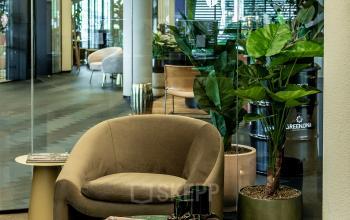 Rent office space at Lange Amerikaweg 55-61 in Apeldoorn featuring a cozy furnished lounge with glass walls, stylish seating, and greenery, ideal for office space rental.