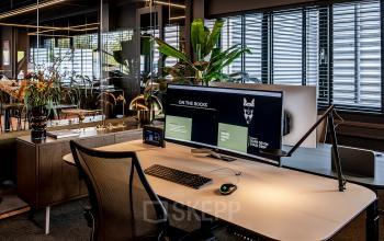 Modern furnished office space available for rent at Lange Amerikaweg 55-61, Apeldoorn. Features ergonomic chair, large monitor, sleek desk, and indoor plants, highlighting an inviting workspace atmosphere.