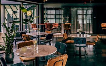 Stylishly furnished office space with round tables, multicolored chairs, and potted plants, ideal for rent at Lange Amerikaweg 55-61, Apeldoorn.