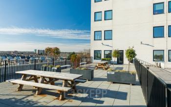 Spacious rooftop terrace at Prins Willem Alexanderlaan 701, Apeldoorn, featuring picnic tables and planters, ideal for informal meetings. Discover this unique office space rental option with stunning city views.