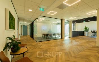 Modern office interior at Prins Willem Alexanderlaan 701, Apeldoorn, featuring a glass-walled conference room and elegant wood flooring. Ideal for office space rental, the area is beautifully lit with contemporary fixtures.