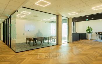Interior view of an office space to rent at Prins Willem Alexanderlaan 701, Apeldoorn, featuring a glass-walled conference room and furnished with modern chairs and tables.