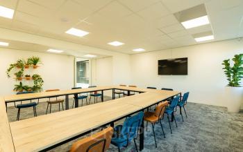 Bright office space rental at Prins Willem Alexanderlaan 701, Apeldoorn, featuring a spacious meeting area with a large rectangular table, colorful chairs, and vibrant plants.