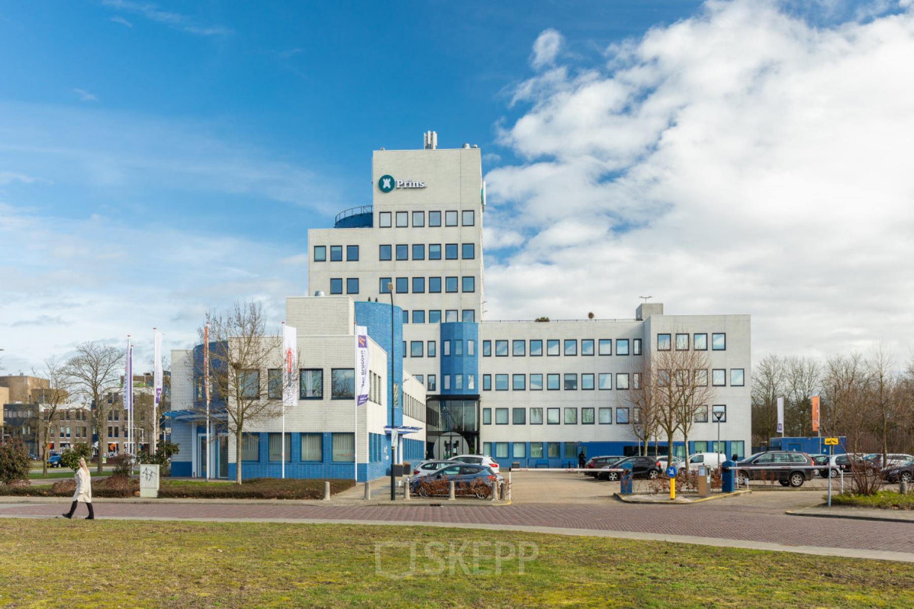 Exterior view of a multi-story office building at Prins Willem Alexanderlaan 701, Apeldoorn, featuring large windows. Ideal for office space rental purposes with convenient access and parking facilities.