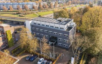 A modern office building located at Waterloseweg 7a in Apeldoorn, featuring multiple stories and large windows, surrounded by trees and a parking area. Ideal for office space rental opportunities.