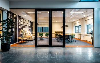 Modern office space with a glass wall, elegant conference table, green chairs, and a comfortable sofa at Waterloseweg 7a, Apeldoorn. Ideal for office space rental.