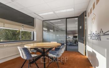 A modern meeting room at Waterloseweg 7a in Apeldoorn, featuring a round wooden table, stylish chairs, and large windows. Ideal for office space rental, complemented by a serene, well-lit environment.