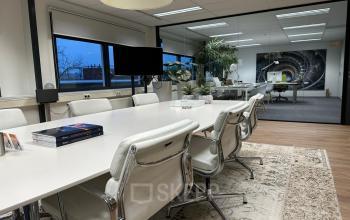 Modern conference room at Waterloseweg 7a, Apeldoorn, featuring a long table surrounded by white chairs and large windows, suitable for meetings or office space rental.