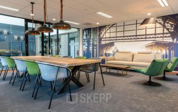 Modern office space at Waterloseweg 7a in Apeldoorn, featuring a stylish conference room with a large wooden table, colorful chairs, and decorative wall art ideal for office space rental.