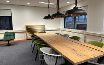 Modern conference room at Waterloseweg 7a, Apeldoorn featuring a long wooden table and stylish chairs, suitable for office space rental. Natural light flows through large windows, enhancing a professional workspace ambiance.