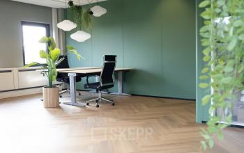 Furnished office space in Apeldoorn with two ergonomic chairs and desks, featuring a green accent wall and natural light. Ideal for office space rental.