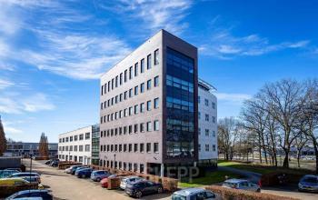 Exterior view of an office building at Schumanpark 9, Apeldoorn, suitable for office space rental, with ample parking space visible.