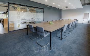 Spacious conference room with a long table, modern chairs, and a glass partition at Oude Apeldoornseweg 41-45. Ideal space for office space rental needs.
