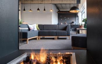 Modern office space at Oude Apeldoornseweg 41-45 in Apeldoorn with contemporary seating and unique lighting fixtures. Discover this inviting office to rent featuring a cozy seating area around a fire.
