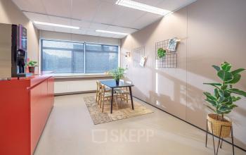 Bright office space with a window, table, chairs, plants, and a red counter, located at Oude Apeldoornseweg 41, Apeldoorn. Ideal for office space rental.