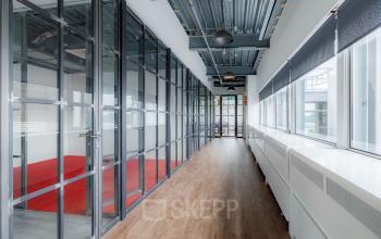 Modern corridor at Oude Apeldoornseweg 41, Apeldoorn, featuring glass-walled office spaces available for rent.