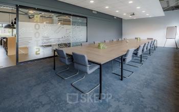 Modern conference room in an office space rental at Oude Apeldoornseweg 41, Apeldoorn, with a long wooden table, grey chairs, and a glass partition wall.