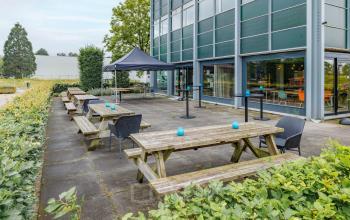 Outdoor seating area with several wooden picnic tables and chairs at the office building located at Oude Apeldoornseweg 41, Apeldoorn.