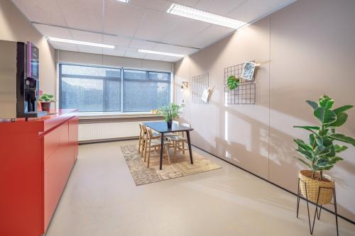 Bright office space with a window, table, chairs, plants, and a red counter, located at Oude Apeldoornseweg 41, Apeldoorn. Ideal for office space rental.