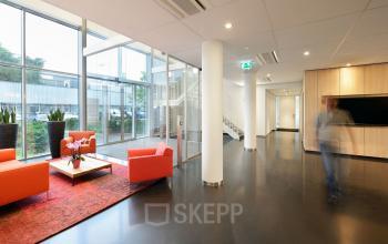 Bright lobby area with red chairs and glass walls at Laan van Malkenschoten 40, Apeldoorn, ideal for office space rental.