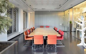 Modern conference room with a long wooden table and vibrant red chairs at Laan van Malkenschoten 40, Apeldoorn. Bright space with large windows and minimalistic decor, available for office space rental.