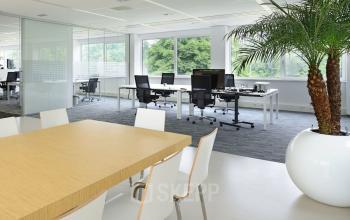 Modern office interior at Laan van Malkenschoten 40, Apeldoorn, featuring large windows, workstations, and a meeting table with white chairs.
