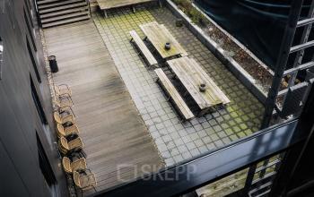 View of an exterior courtyard at Roggestraat 111, Apeldoorn, featuring wooden benches and chairs arranged for seating, ideal for breaks or outdoor meetings.