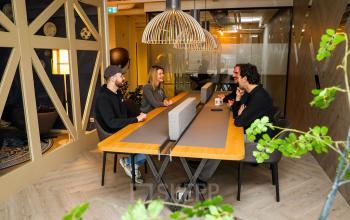 Modern furnished office space at Roggestraat 111, Apeldoorn with four people having a team meeting around a wooden table.