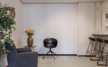 Interior of office space at Roggestraat 111, Apeldoorn, featuring modern chairs, a table with stools, and a decorative plant.